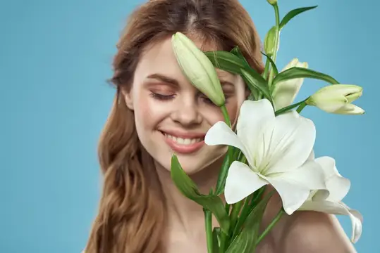 Улыбающаяся девушка с белыми лилиями у лица на голубом фоне