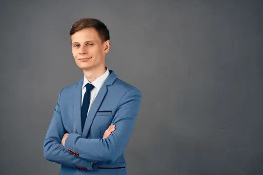 Уверенный молодой человек в синем костюме на сером фоне