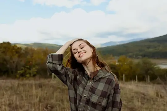 Молодая женщина с закрытыми глазами отдыхает на природе в клетчатой рубашке