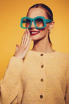 Улыбающаяся женщина в больших бирюзовых очках на жёлтом фоне