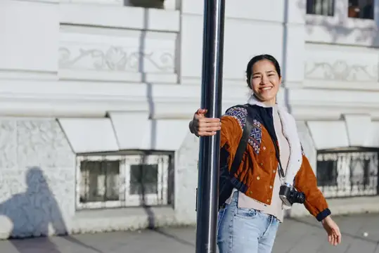 Улыбающаяся азиатская девушка с фотоаппаратом у фонарного столба