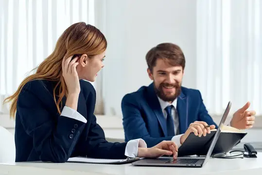 Улыбающиеся коллеги обсуждают проект за ноутбуком в офисе