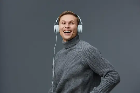 Улыбчивый мужчина в наушниках слушает музыку на сером фоне