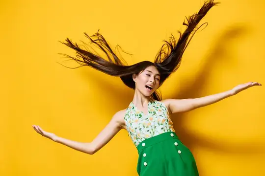 Азиатская девушка в прыжке с развевающимися волосами на жёлтом фоне