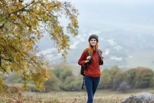 Рыжеволосая девушка с рюкзаком гуляет по осеннему лесу