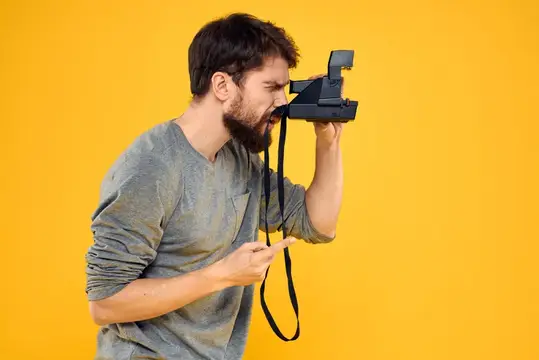 Бородатый мужчина с ретро-фотоаппаратом на жёлтом фоне