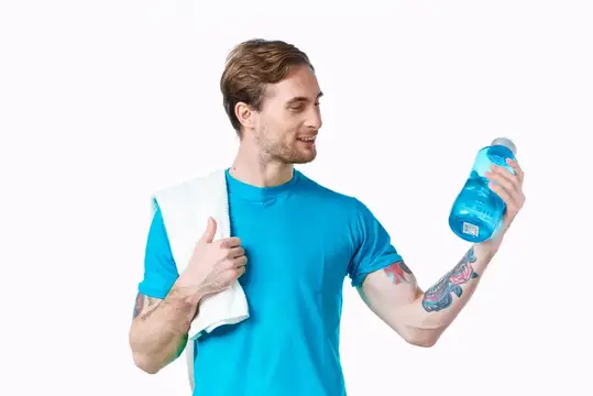 Молодой мужчина с татуировками держит бутылку воды и полотенце