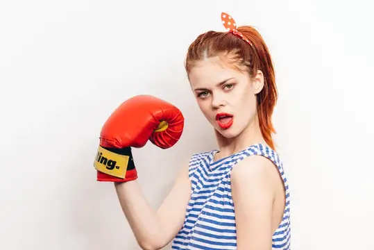 Активная женщина занимается боксом в красных перчатках и полосатой футболке на светлом фоне