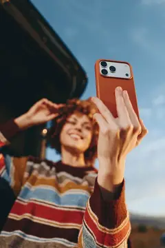 Женщина в полосатом свитере делает селфи на улице, держа смартфон высоко