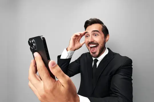 Удивлённый мужчина в костюме смотрит в смартфон и кричит от восторга