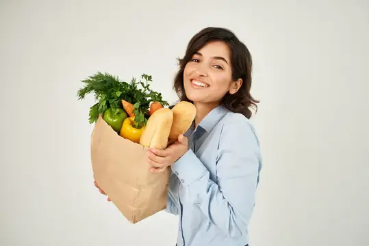 Веселая женщина с пакетом продуктов из супермаркета покупает овощи