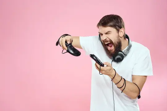 Бородатый мужчина в наушниках яростно играет в видеоигру на розовом фоне