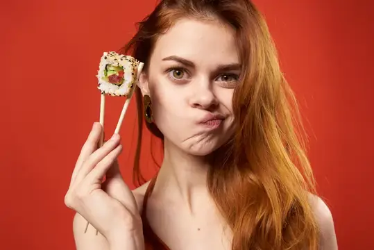 Жизнерадостная женщина ест суши, азиатская еда, красный фон