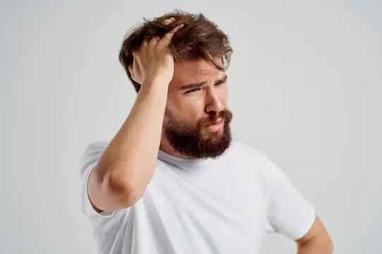 Задумчивый бородатый мужчина чешет затылок на сером фоне