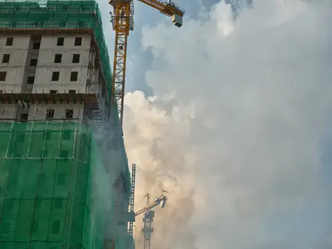 Строительная площадка с зеленым зданием, кранами и облачным небом, демонстрирующая городское развитие и архитектуру