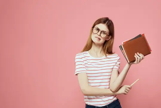 Студентка с блокнотами на розовом фоне жестикулирует руками