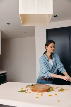 Молодая женщина в джинсовой рубашке режет овощи на кухне