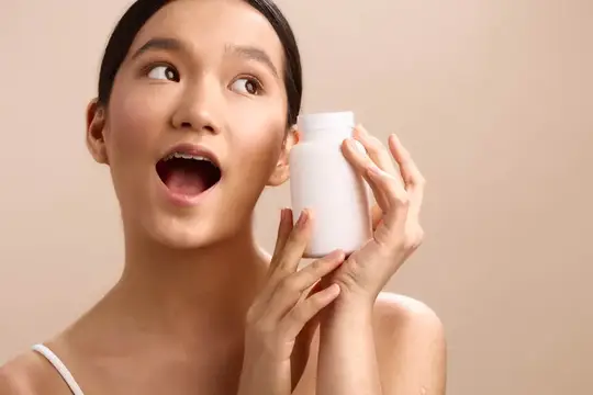 Удивлённая азиатская девушка с белым флаконом в руках