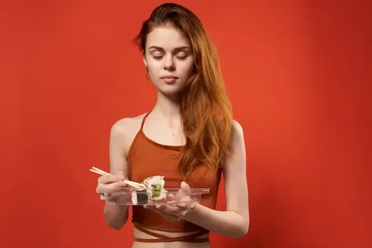 Милый рыжеволосая женщина с палочками для суши, роллами и морепродуктами в качестве закуски