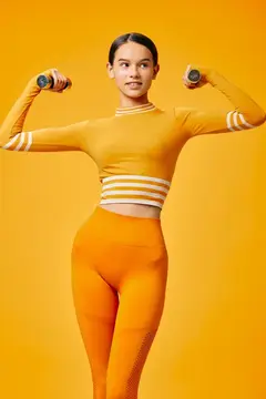 Спортивная девушка с гантелями позирует на оранжевом фоне