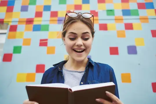 Улыбающаяся девушка с книгой на фоне разноцветной стены