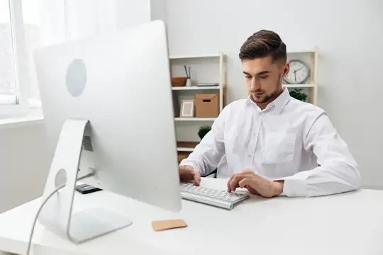 Молодой мужчина в белой рубашке работает за компьютером в офисе