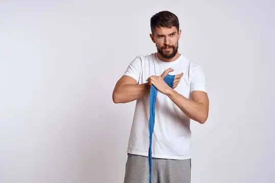 Спортивный мужчина в белой футболке с синими боксёрскими бинтами на руках, выполняет тренировочные упражнения