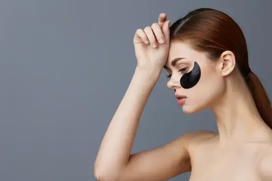 Молодая женщина с черными патчами под глазами на сером фоне