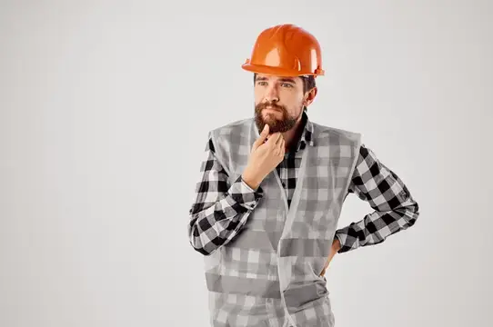 Задумчивый бородатый мужчина в оранжевой каске и сером жилете
