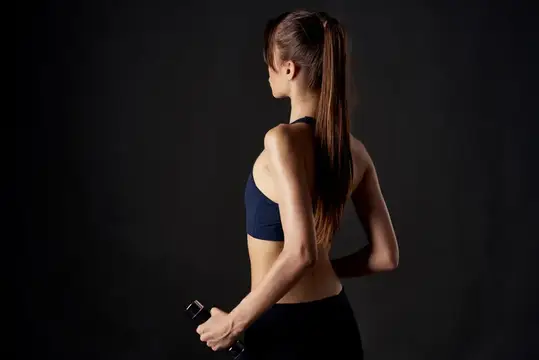 Спортивная девушка с гантелью на тёмном фоне