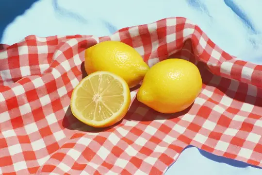 Спелые лимоны и половинка фрукта на красно-белой клетчатой ткани