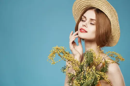 Молодая женщина в соломенной шляпе с ветками мимозы на голубом фоне