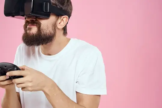 Бородатый мужчина в VR-очках с геймпадом на розовом фоне