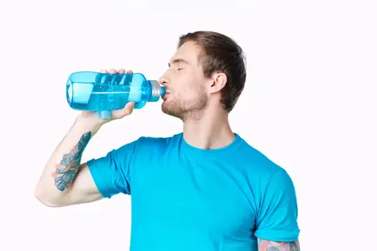Спортсмен пьет воду из бутылки на белом фоне