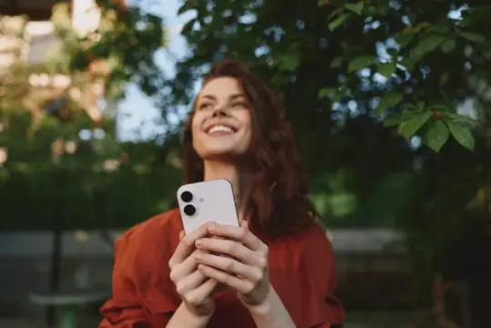 Улыбающаяся темноволосая девушка со смартфоном в руках на фоне зелени