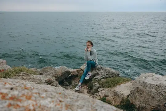 Женщина в свитере любуется морем и облаками, наслаждаясь природой