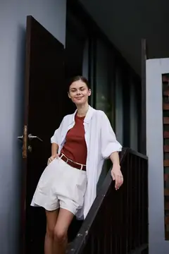 Улыбающаяся девушка в белой рубашке стоит у открытой двери