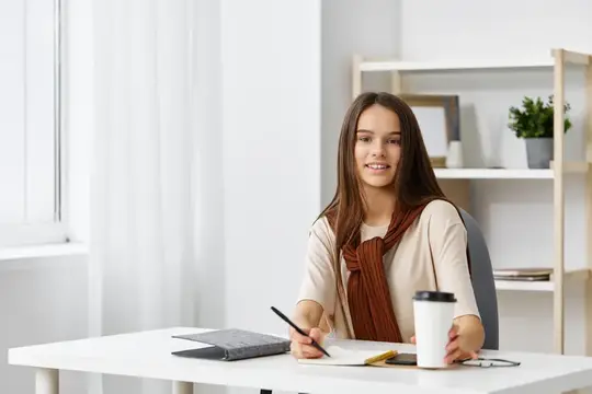Молодая женщина с блокнотом улыбается за белым столом в светлой комнате