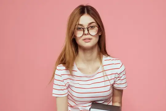 Молодая студентка с книгами на розовом фоне, в очках на лице, кадрированный вид, учебное заведение
