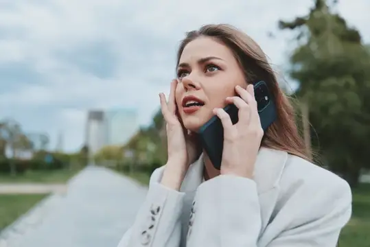 Испуганная женщина в светлом пиджаке говорит по телефону на улице