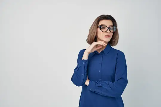 Задумчивая женщина в очках и синей рубашке на светлом фоне