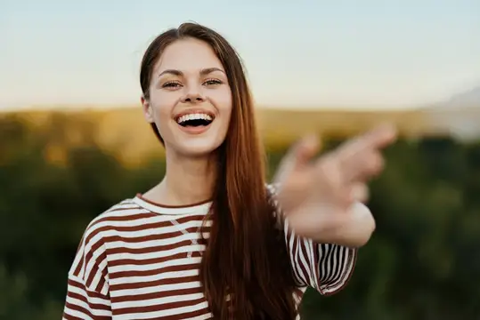 Улыбающаяся девушка с длинными волосами протягивает руку на фоне заката