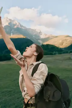 Девушка с рюкзаком делает селфи на фоне гор