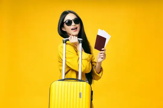 Улыбающаяся темноволосая девушка с чемоданом и паспортом на жёлтом фоне
