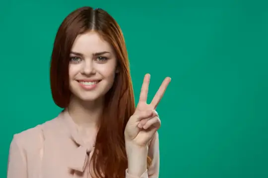 Улыбающаяся рыжеволосая девушка показывает жест победы на зелёном фоне
