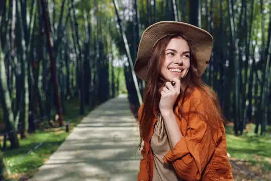 Улыбающаяся девушка в шляпе и оранжевой рубашке на тропинке в бамбуковом лесу