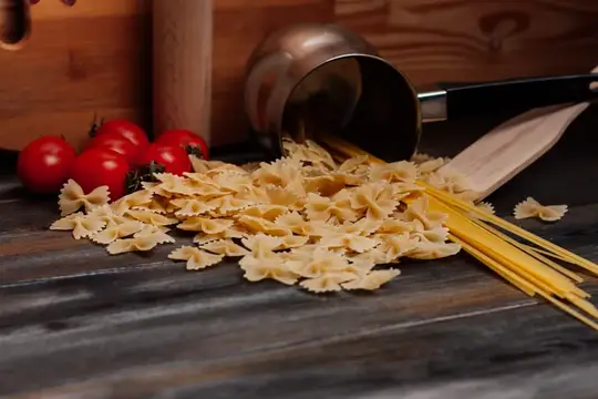 Сырые макароны бантики и спагетти рассыпаны на деревянном столе рядом с помидорами
