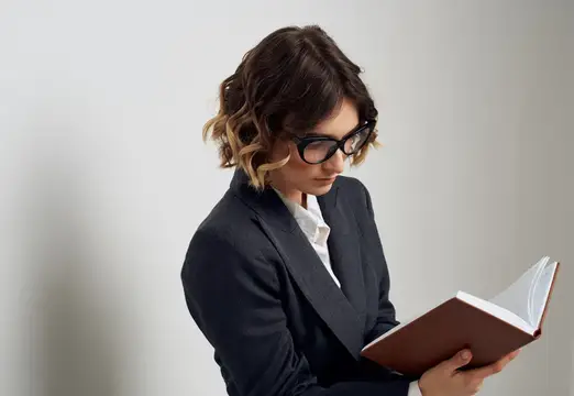 Деловая женщина в очках, с книгой в руках, в классическом костюме, закрывает лицо руками