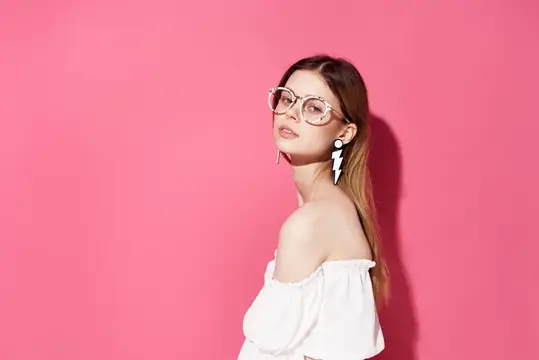 Молодая женщина в очках и белой блузе на розовом фоне