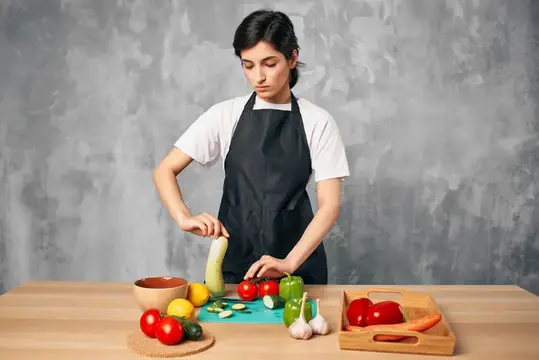 Молодая женщина в чёрном фартуке режет кабачок на кухне